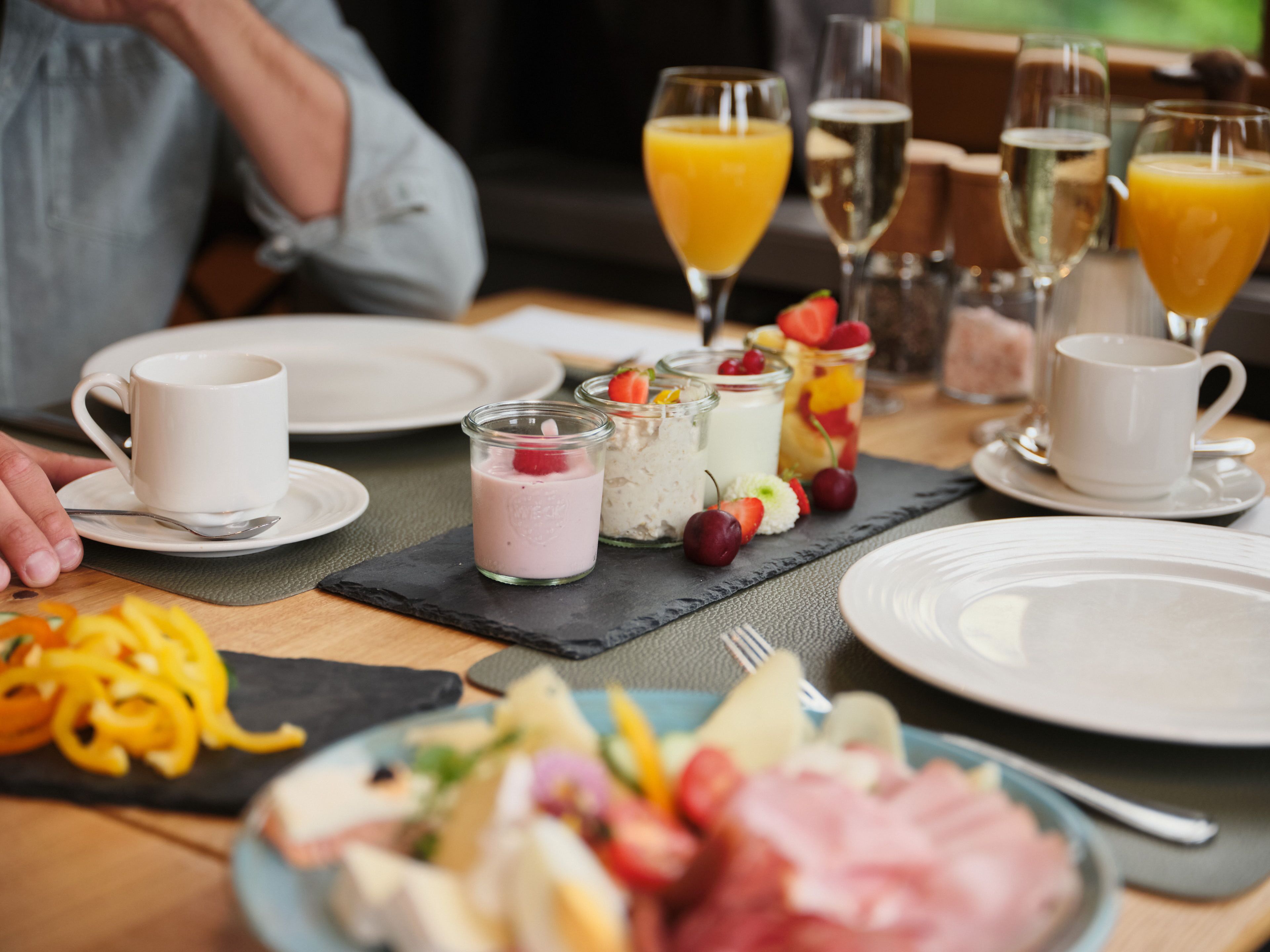 A breakfast setting with various dishes, including fruits, yogurt, and a plate of ham.