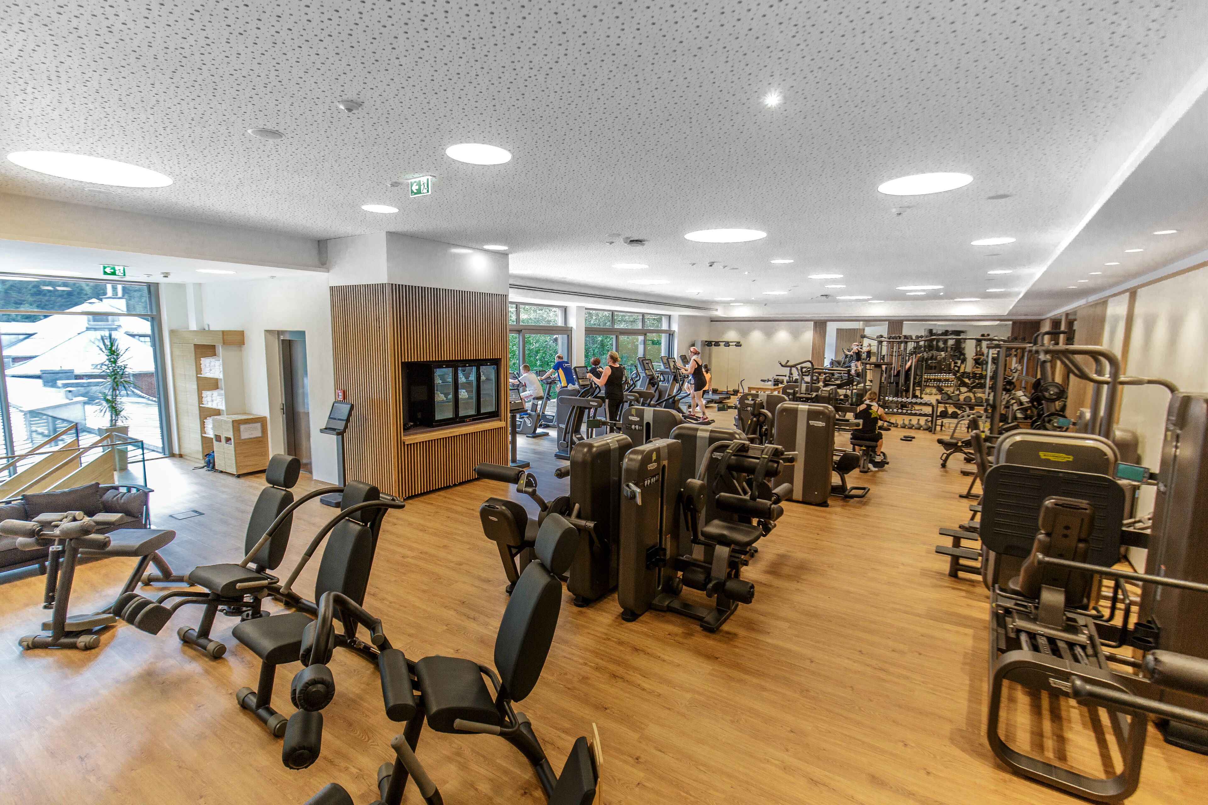 Ein Fitnessstudio mit verschiedenen Trainingsgeräten, einem Fernseher und großen Fenstern.