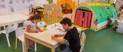 A classroom with children and an adult at a table, surrounded by educational posters and a play area.