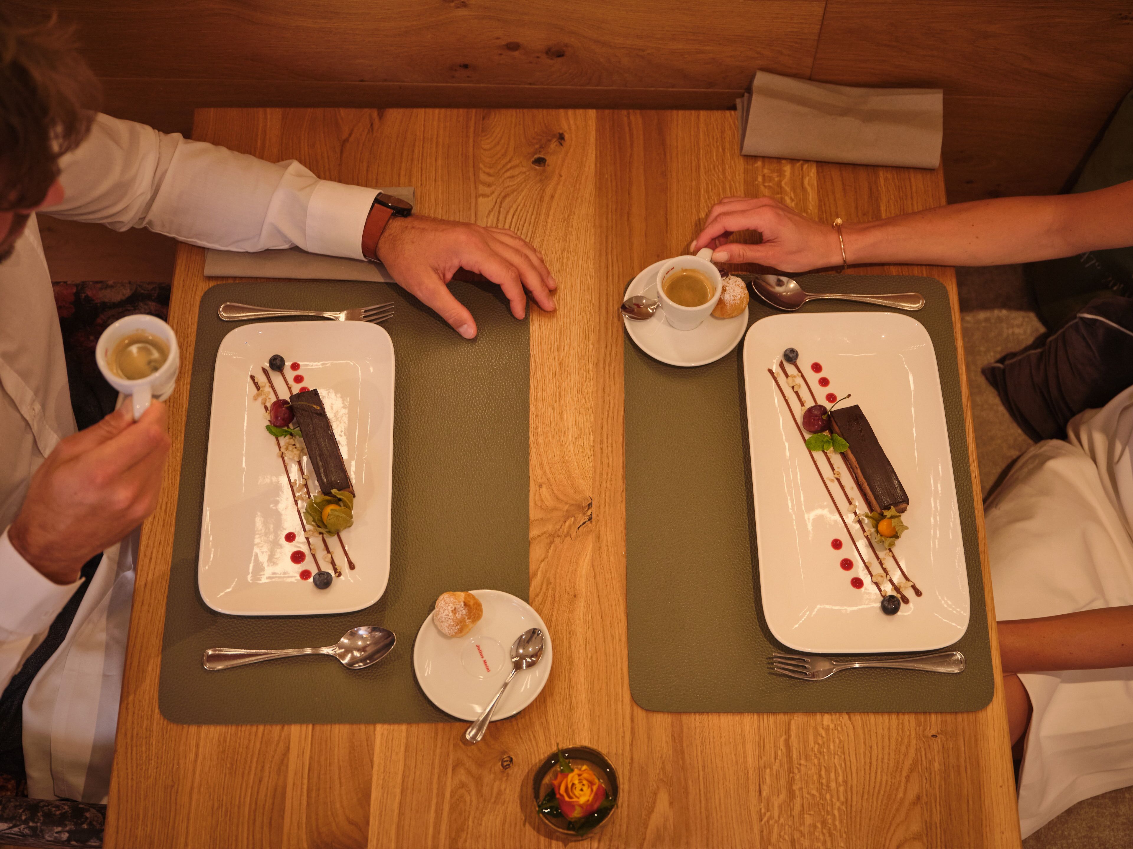 Una mesa de comedor con dos platos rectangulares de postre, cada uno con una cuchara y una taza de café.