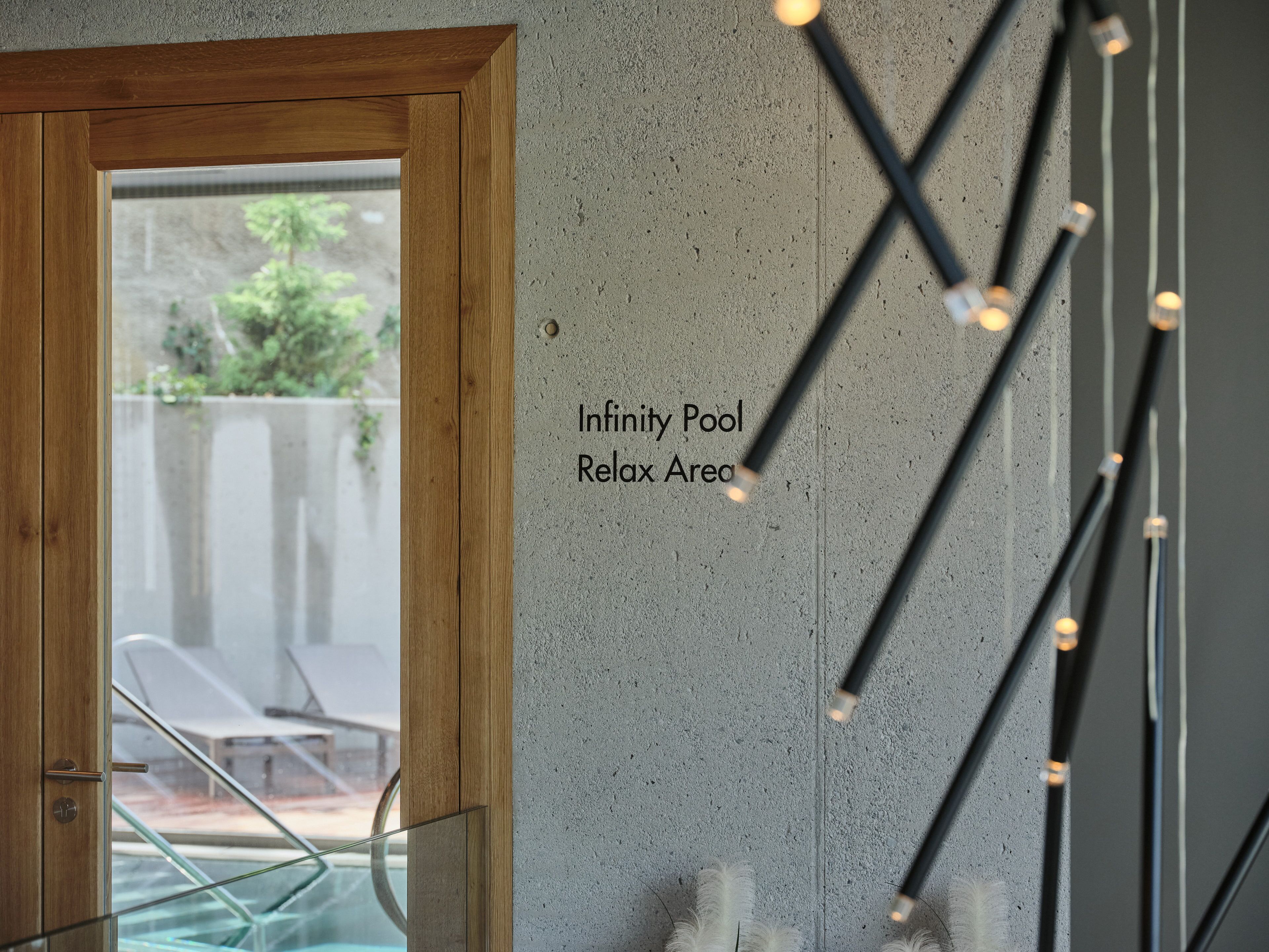 A view of a room with a wooden door leading to a glass door, a concrete wall, and a sign that reads "Infinity Pool Relax Area".