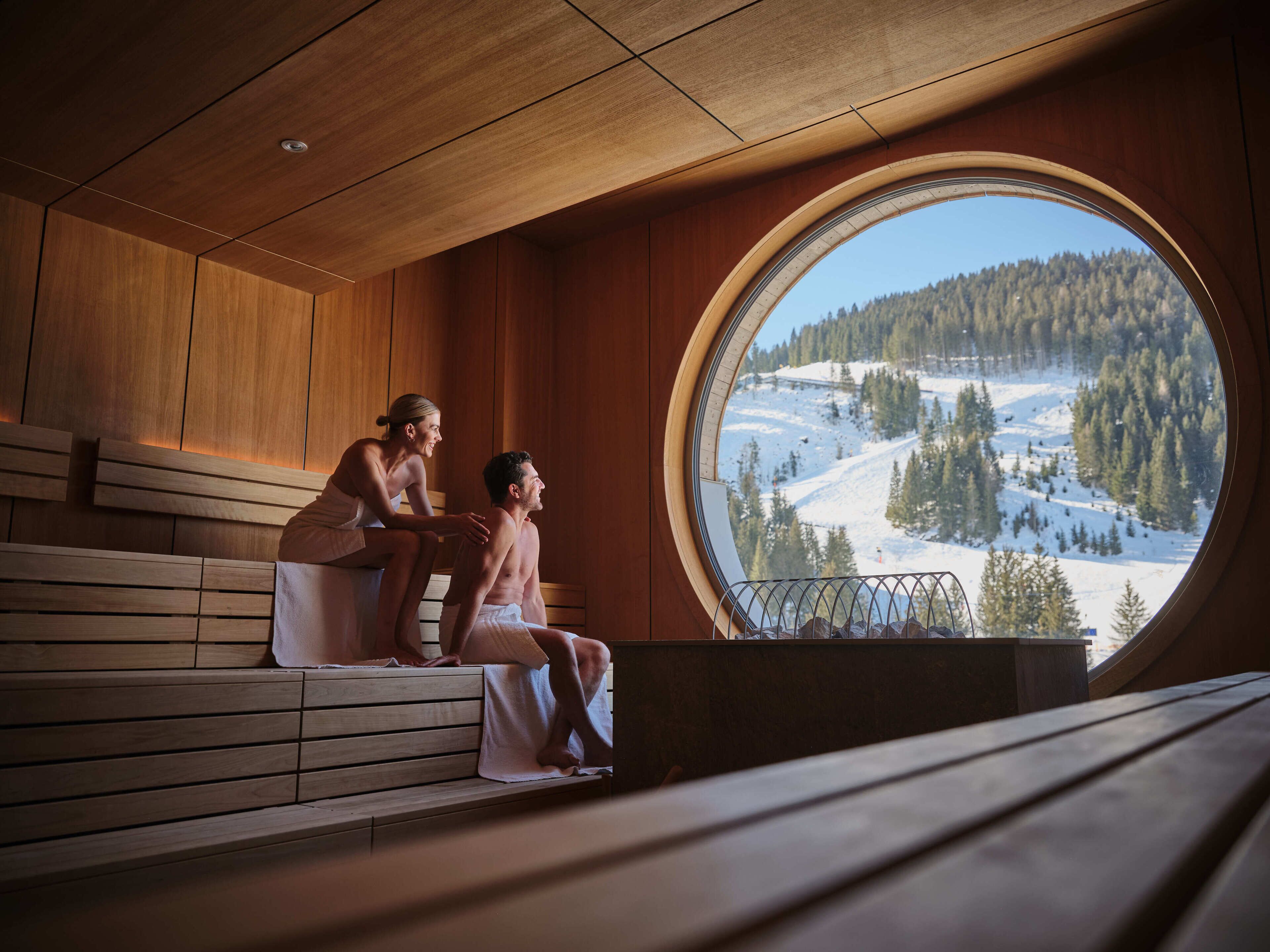 A wooden sauna with a large window offering a view of a snowy mountain landscape.