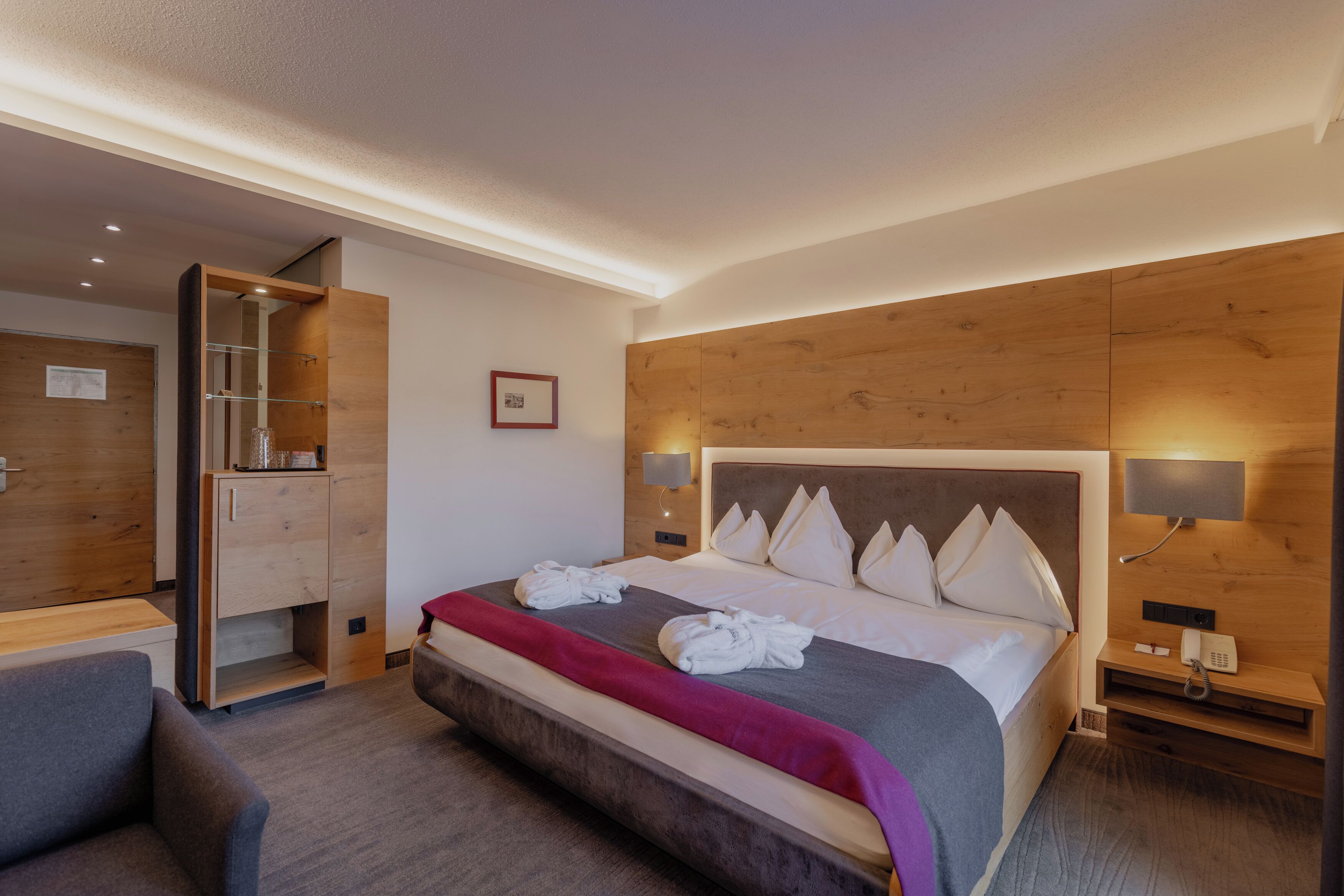 A hotel room with a bed, bedside tables, a wardrobe, and a desk.