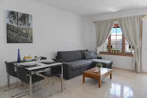 Un salon moderne comprenant un canapé, une table basse, une table à manger avec des chaises et une fenêtre avec des rideaux.