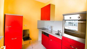 A compact kitchen with red cabinets, a stainless steel oven, and a black chair. - T1-Apartment-1.OG-HH (Bergisch Gladbach)