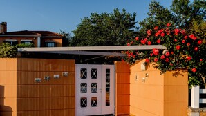 A modern building with a wooden facade, a white door with glass panels, and a garden with red flowers. - AR apartment (Πλατανίδια)