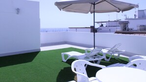 A rooftop terrace with artificial grass, white lounge chairs, and a table under a large umbrella. - Mele Sky Beach, BEACH APARTMENT, sea views, terrace and sun (Lomo Quiebre)
