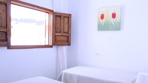 A bedroom with two beds, a window with wooden shutters, and a painting of red tulips on the wall. - Mele Sky Beach, BEACH APARTMENT, sea views, terrace and sun (Lomo Quiebre)