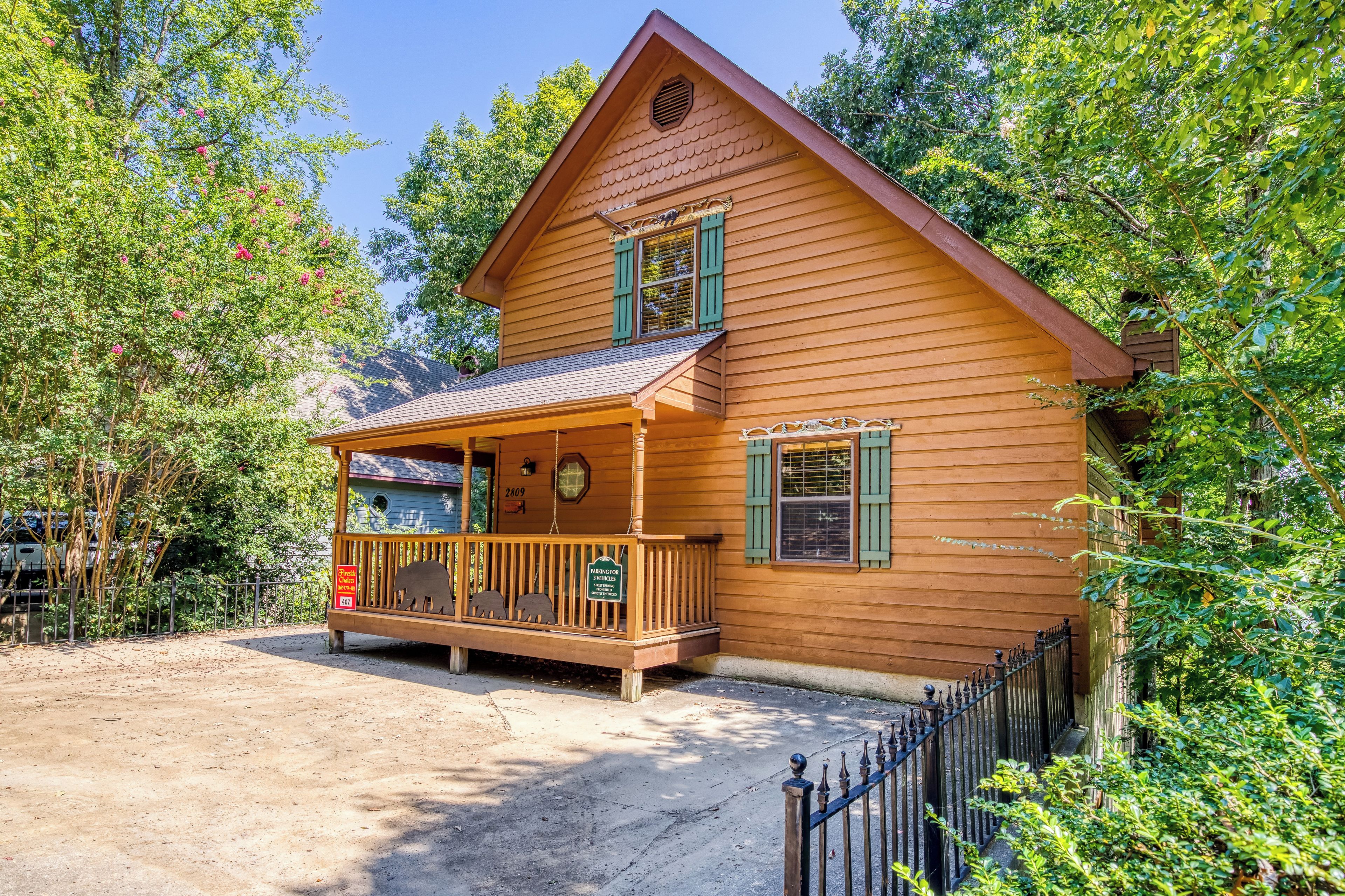 Een houten chalet met een veranda, een klein bijgebouw en een omheinde oprit.
