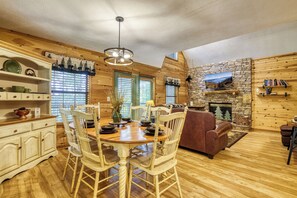 A cozy cabin interior with a dining area, wooden walls, a stone fireplace, and a bookshelf. - 1 mile from Pigeon Forge, outdoor Fireplace Outdoor pool access-game room & More (Pigeon Forge)