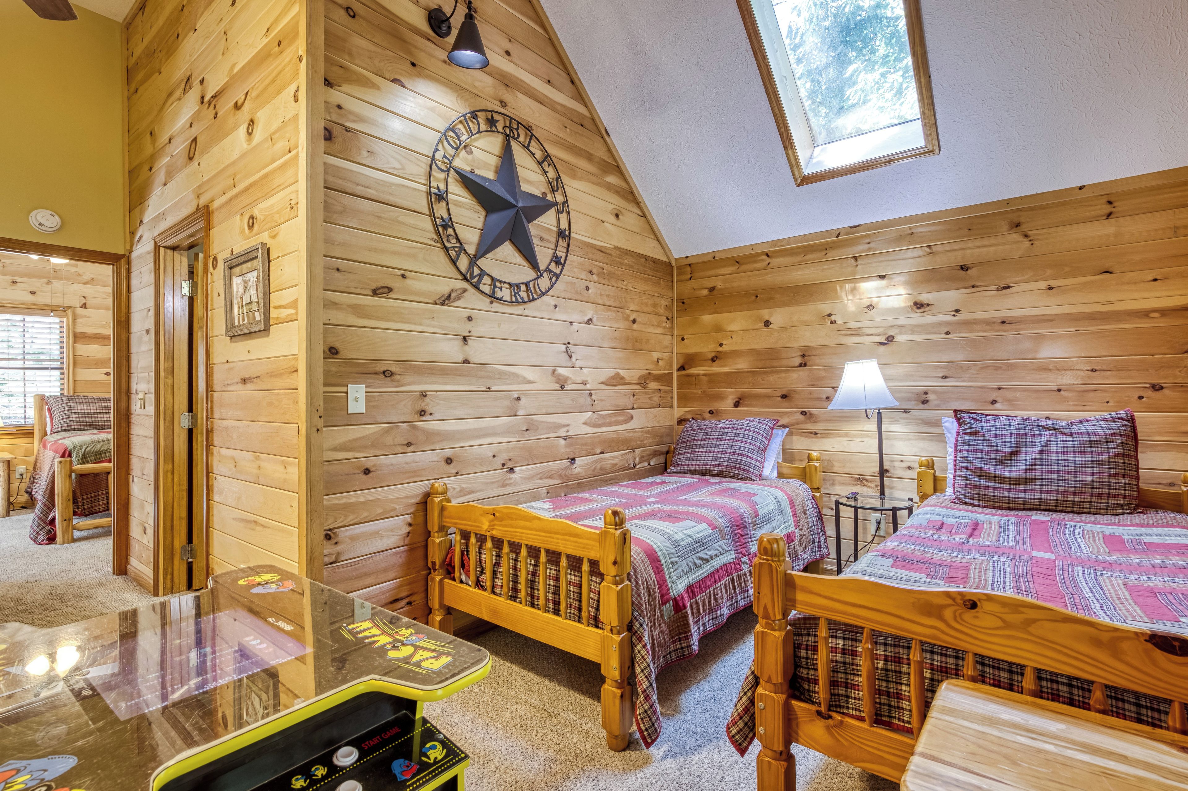A cozy log cabin room with two wooden beds, a ceiling fan, a star decoration, and a small table with a video game console.