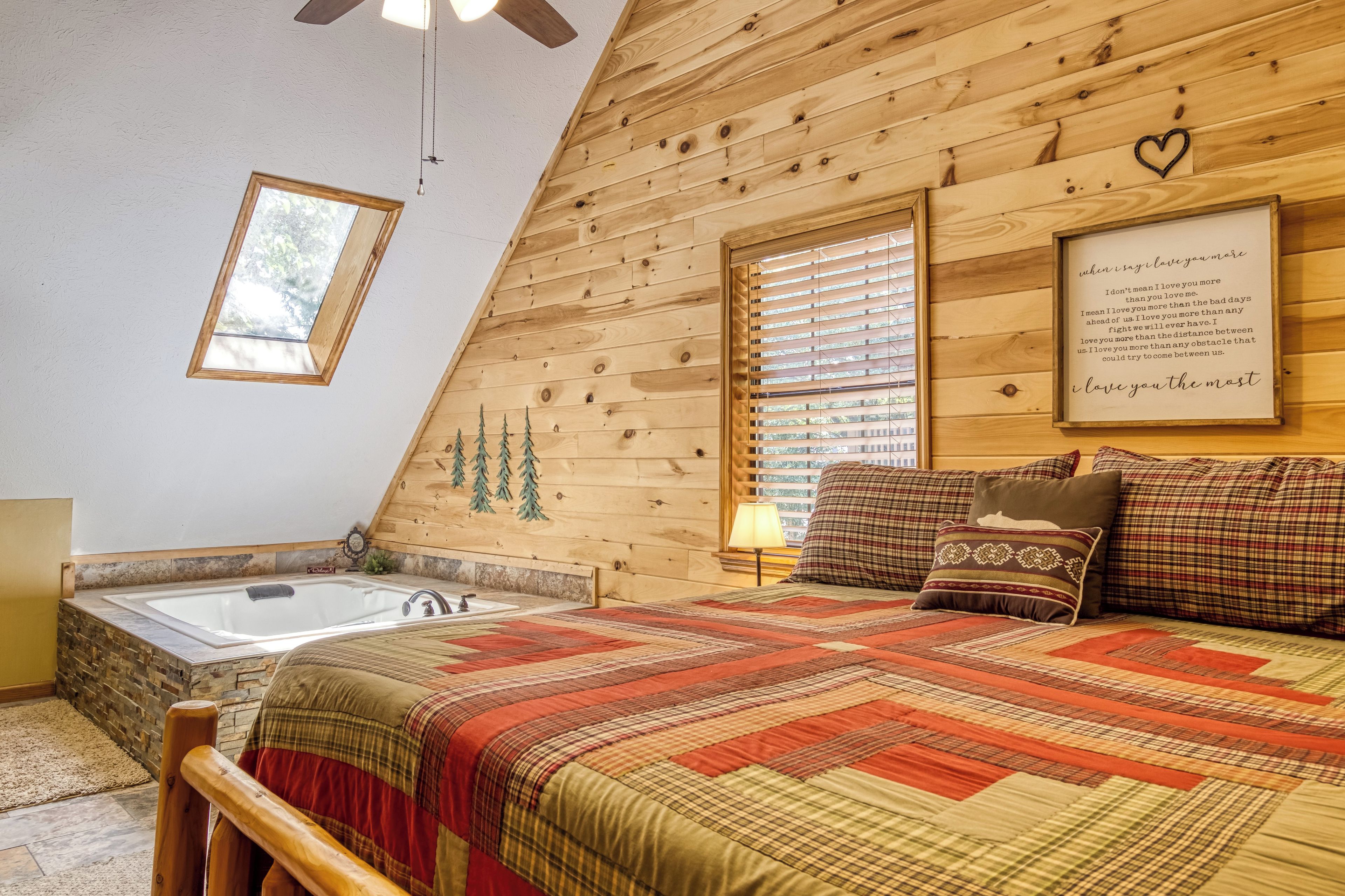A bedroom with a wooden sloped ceiling, a bed with a quilt, a window with blinds, a wall-mounted heart-shaped decoration, and a framed quote.