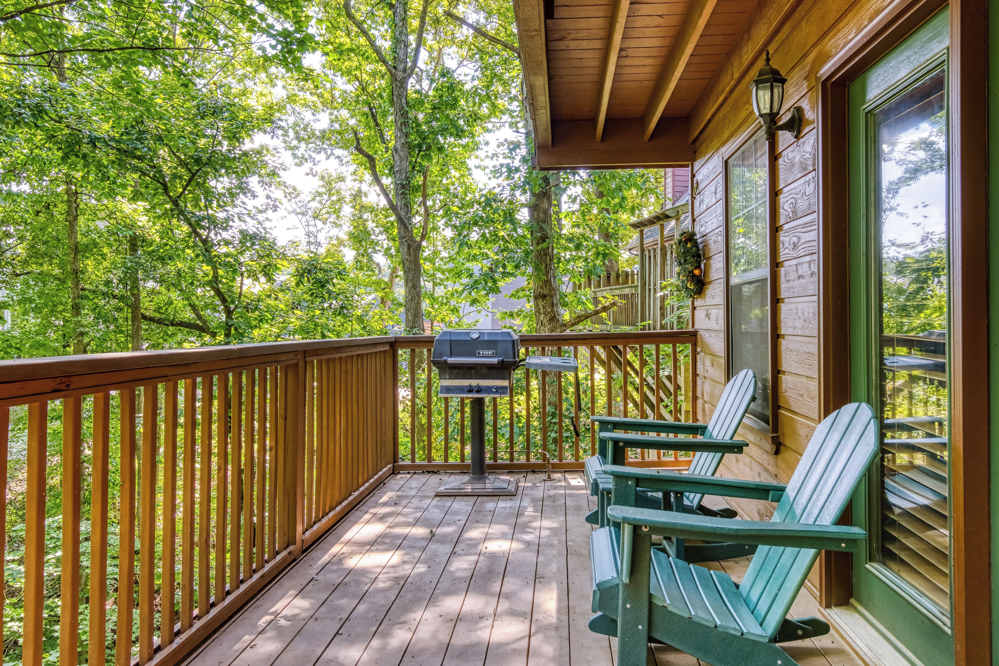 Una terraza de madera con una parrilla, dos sillas Adirondack y vistas a un bosque.