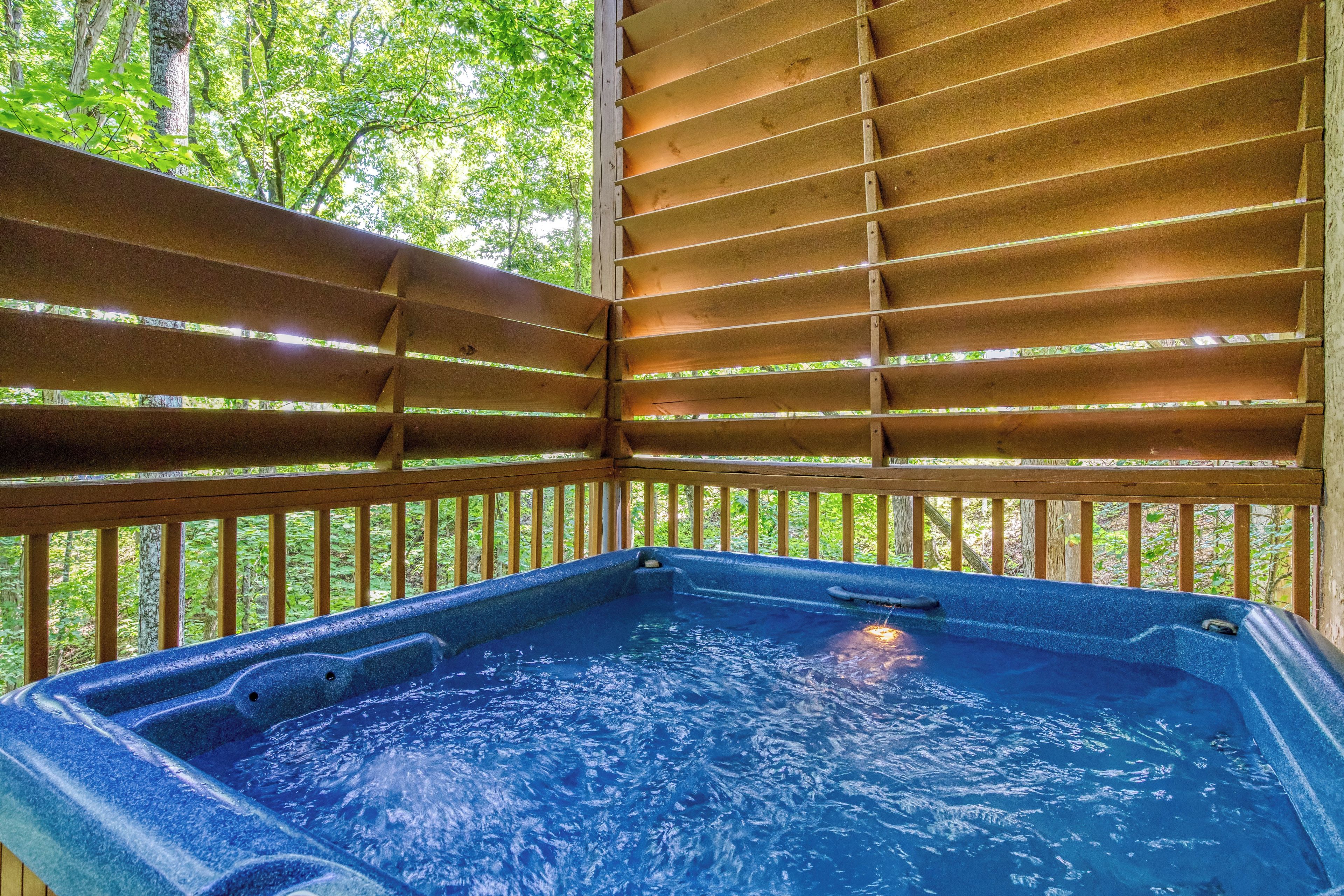 A hot tub with a wooden deck and railings, surrounded by trees.