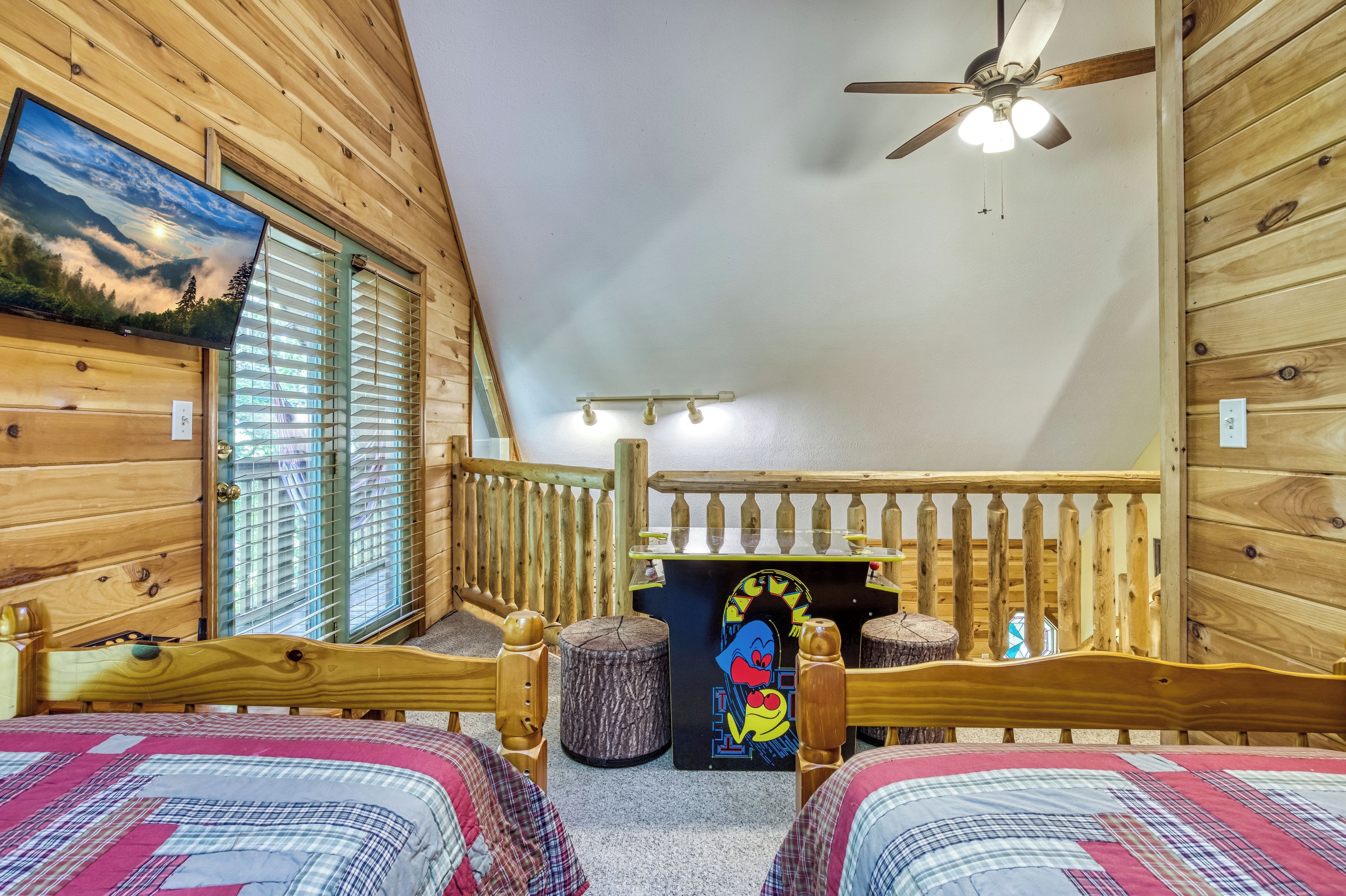 Ein gemütliches Zimmer mit Holzwänden, einem Deckenventilator, einem Bett mit farbenfroher Steppdecke und einem Fenster mit Jalousien.