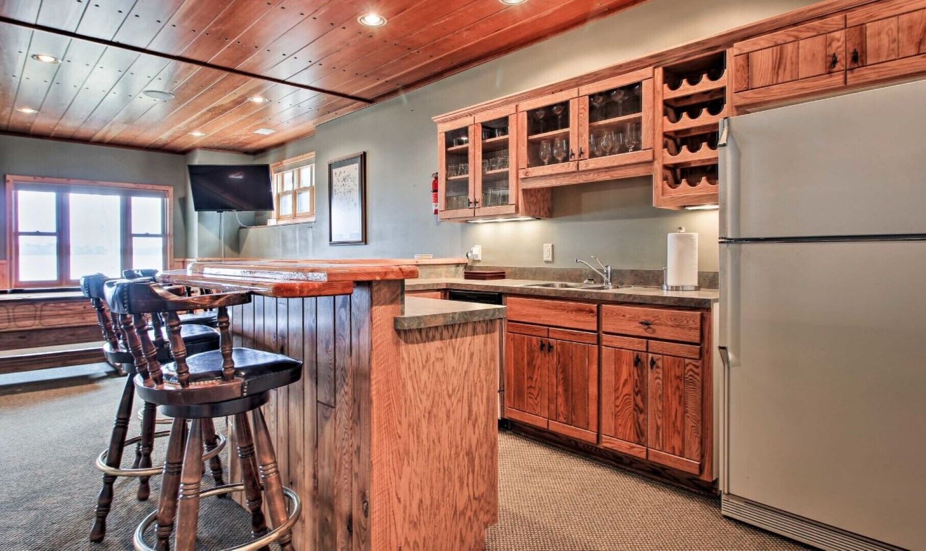 A kitchen with wooden cabinets, a bar area with stools, and a large window.