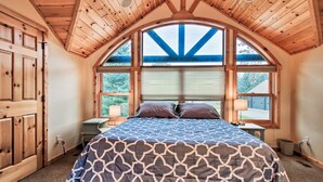 A bedroom with a large bed, wooden ceiling, and a view through a large window. - Bay Lake Cabin w/200ft of Lakefront, fun deck, private dock + woodfire sauna!  (Deerwood)