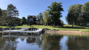 A lakeside property with a dock, a large house with a balcony, and a well-maintained lawn. - Bay Lake Cabin w/200ft of Lakefront, fun deck, private dock + woodfire sauna!  (Deerwood)
