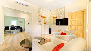 Un salon moderne avec un canapé blanc, une table basse en verre et un mur d’accent en pierre. On aperçoit à l’arrière-plan un coin repas avec une table et des chaises.