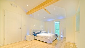 Une chambre avec un plancher en bois, un lit avec une literie blanche, une table de chevet et une fenêtre avec des rideaux.