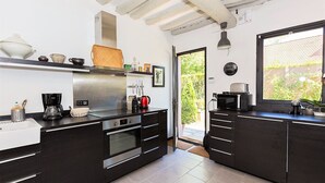 Une cuisine moderne avec des meubles de couleur sombre, des appareils en acier inoxydable et une grande fenêtre offrant une vue sur la verdure environnante.