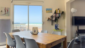 Un espace repas moderne avec une table en bois et des chaises grises, donnant sur une plage.