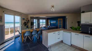 Une cuisine moderne dotée d’un îlot central, d’un coin repas avec des chaises et d’une vue sur l’océan grâce à de grandes portes coulissantes.