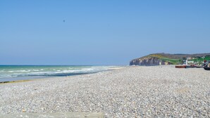 Une plage de galets, avec une falaise rocheuse en arrière-plan et un ciel dégagé.