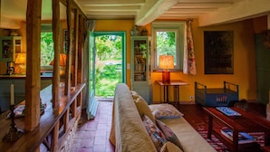 Habitació acollidora amb una banca de fusta, un sofà i una taula petita plena de llibres. Hi ha una porta que dóna a un jardí.