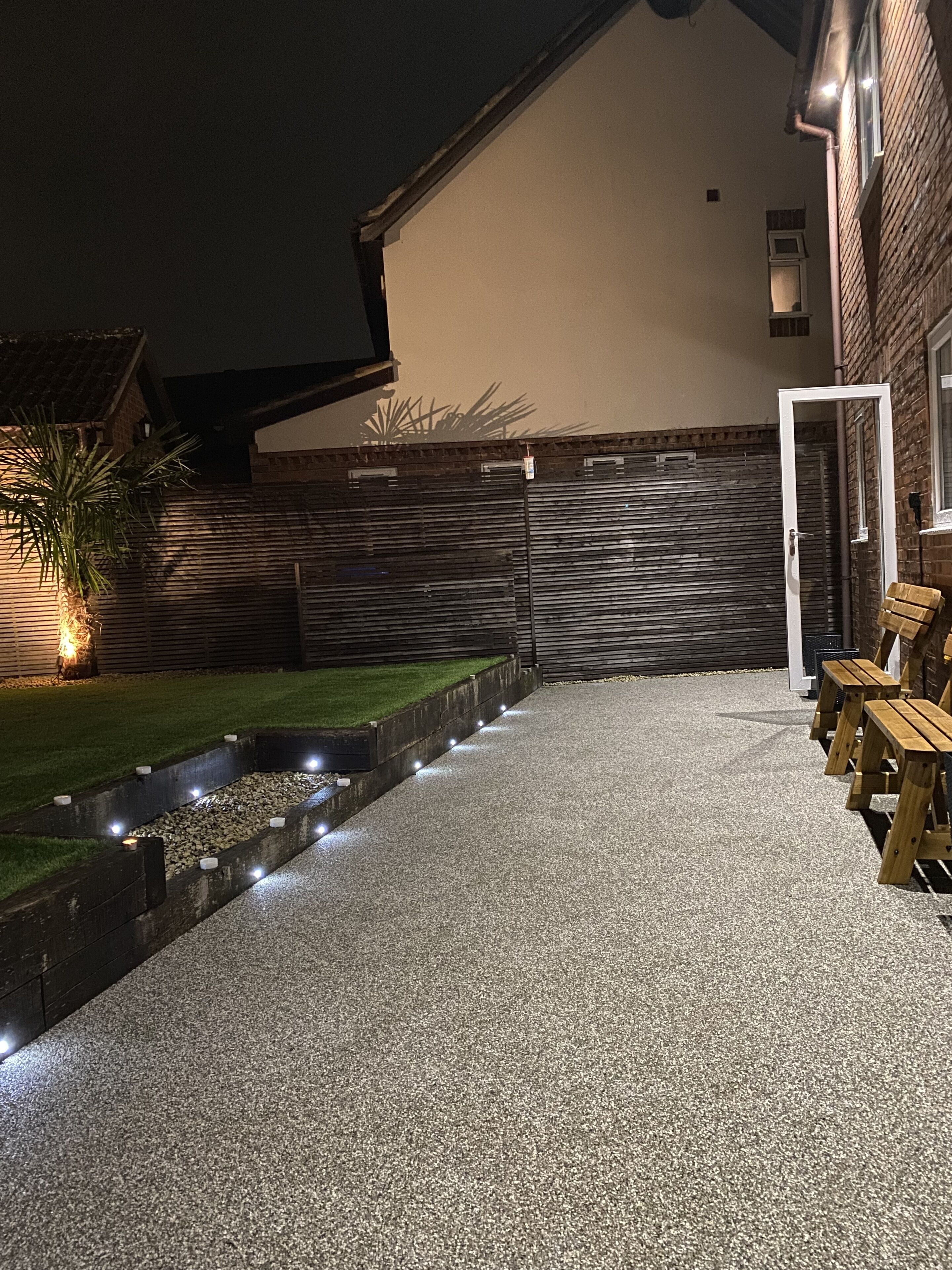 A paved patio with a small water feature, wooden benches, and a brick wall.