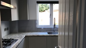 A compact kitchen with grey cabinets, a marble countertop, a built-in gas stove, and a window with a view of greenery outside.