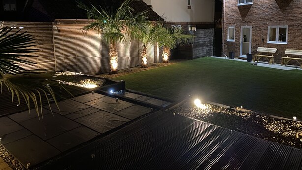 A well-lit backyard with a patio, a lawn, and a brick house.