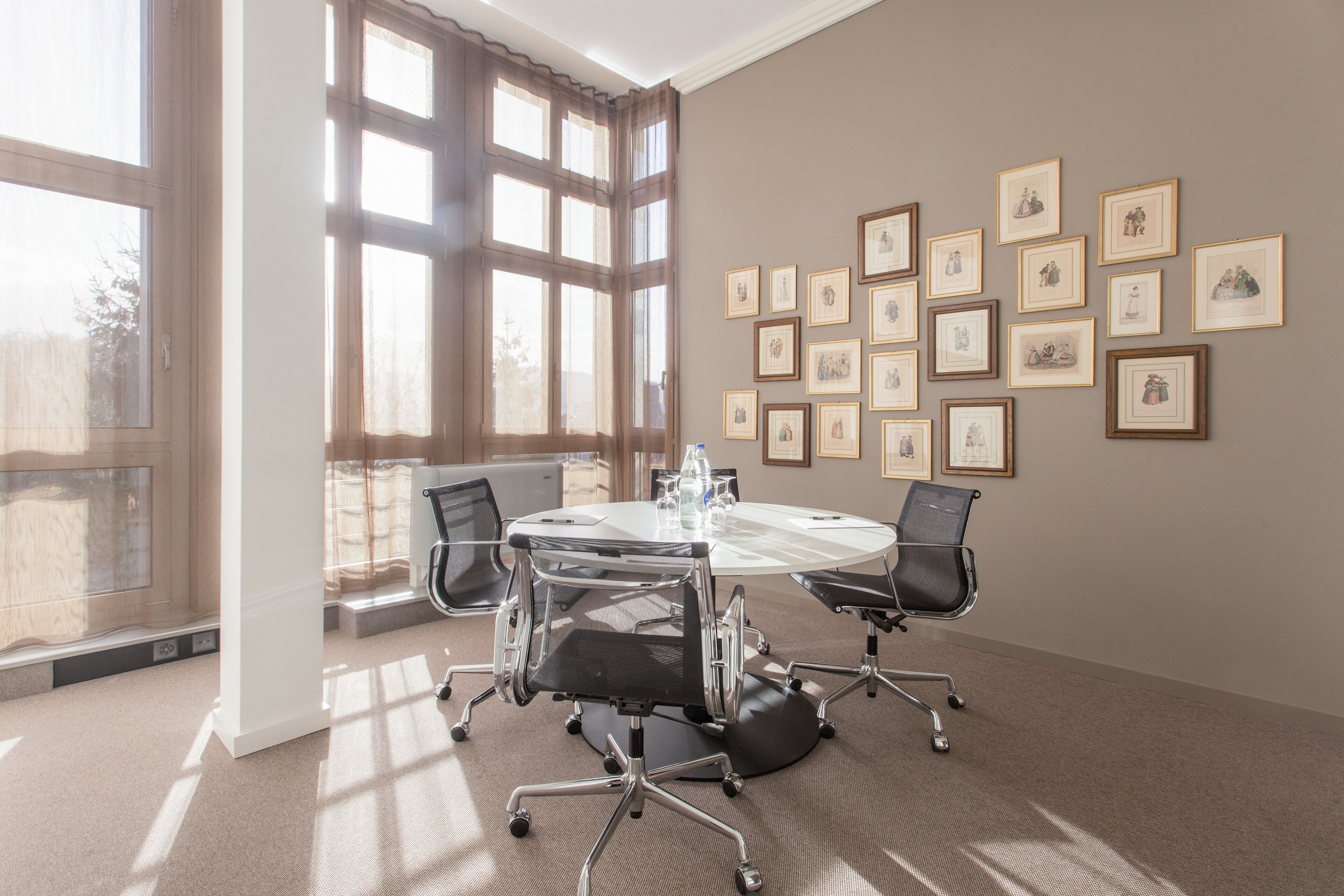 A conference room with a round table, four chairs, and framed pictures on the wall.