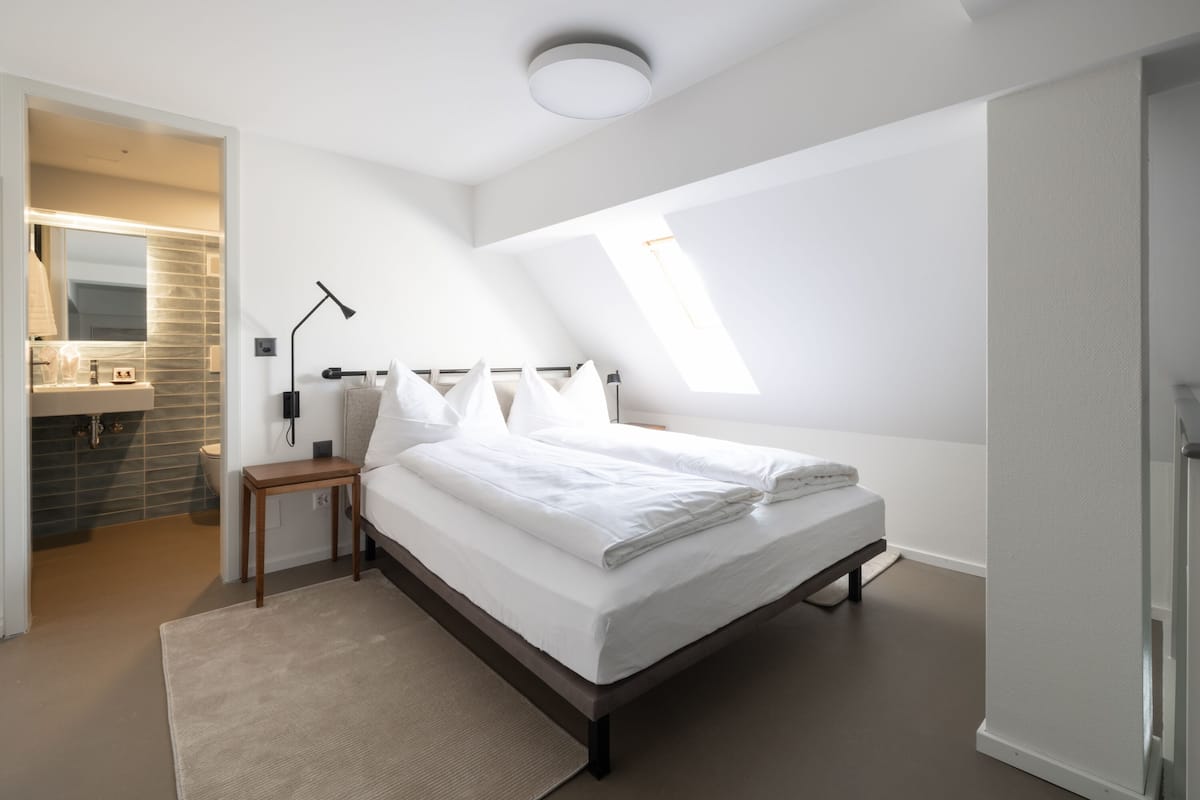 Ein modernes Schlafzimmer mit einem großen Bett, einem Nachttisch, einem Spiegel und einem Oberlicht.