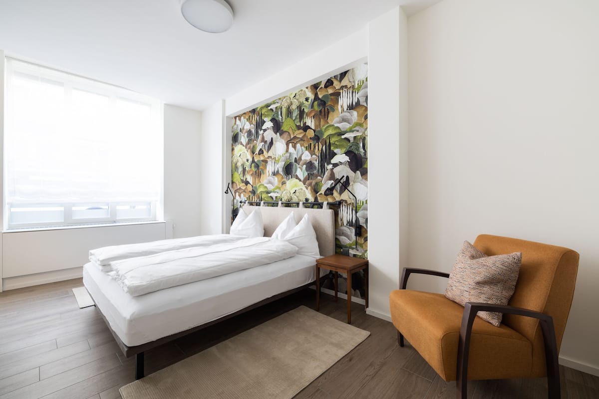 Ein Schlafzimmer mit einem Bett, einem Sessel, einem Nachttisch und einer großen Blumenmalerei an der Wand.
