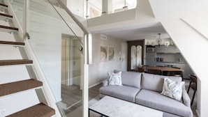 Un interior moderno con una escalera, una sala de estar con sofá y una cocina al fondo.