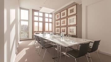 Ein Konferenzraum mit einem langen Tisch, Stühlen, gerahmten Bildern an der Wand und großen Fenstern.