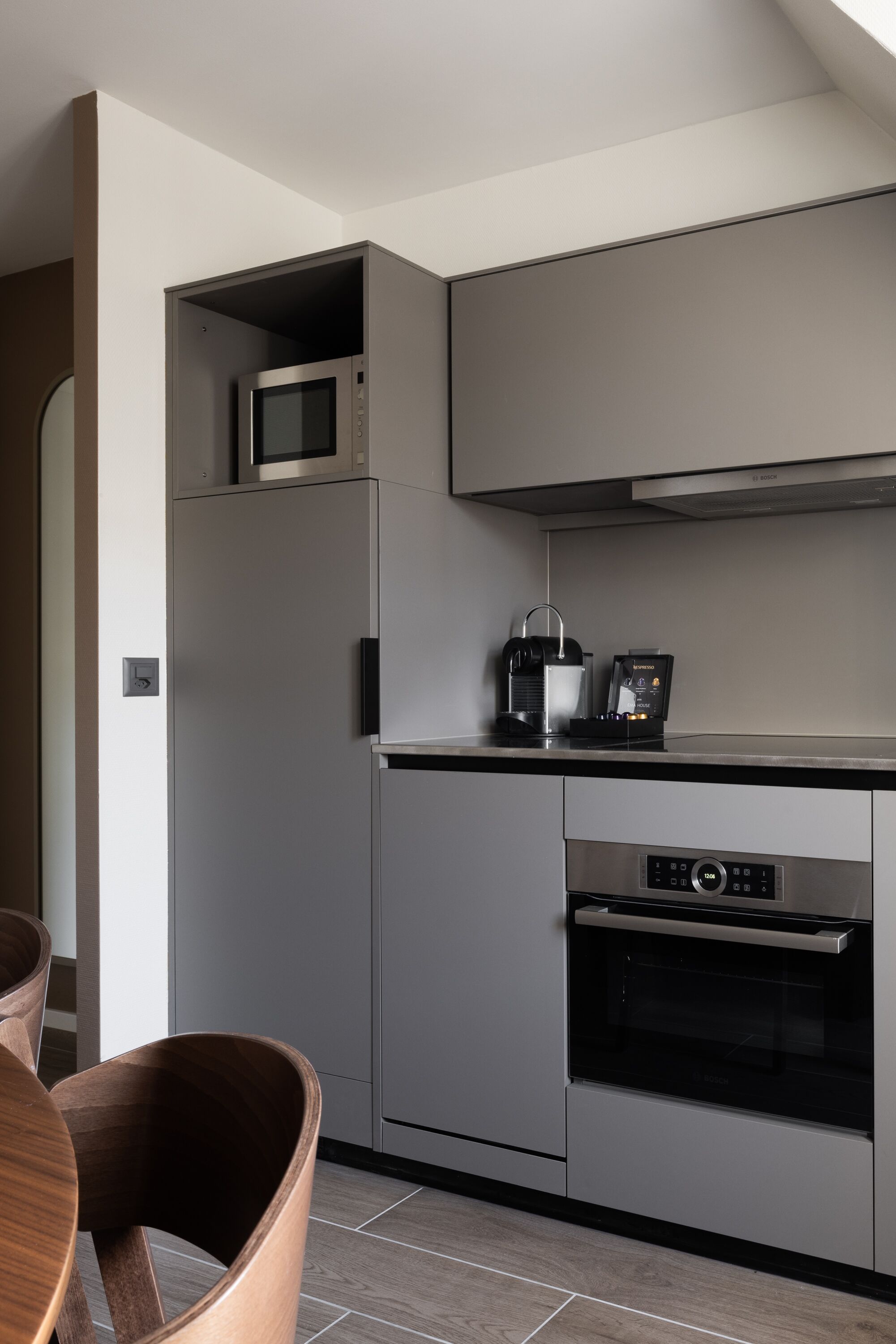 Une cuisine moderne avec des meubles de couleur grise, un four à micro-ondes encastré, une machine à café et un four.
