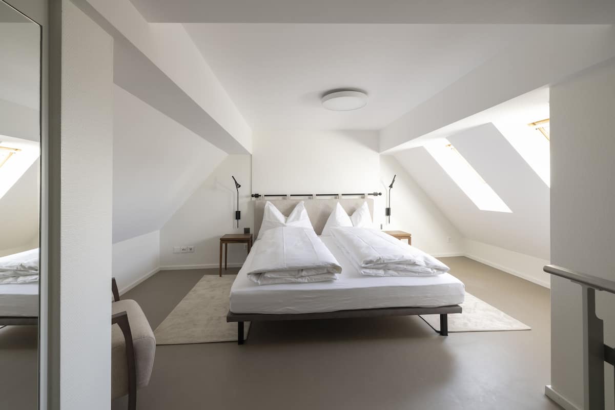 Ein Schlafzimmer mit Bett, Sessel, Nachttisch und Dachfenster.