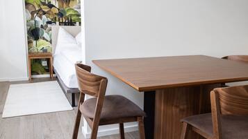 Ein moderner Essbereich mit einem Holztisch und Stühlen, einem weißen Teppich und einem Bett, dessen Wand hinter dem Bett einen grün-weißen Musteraufdruck hat.