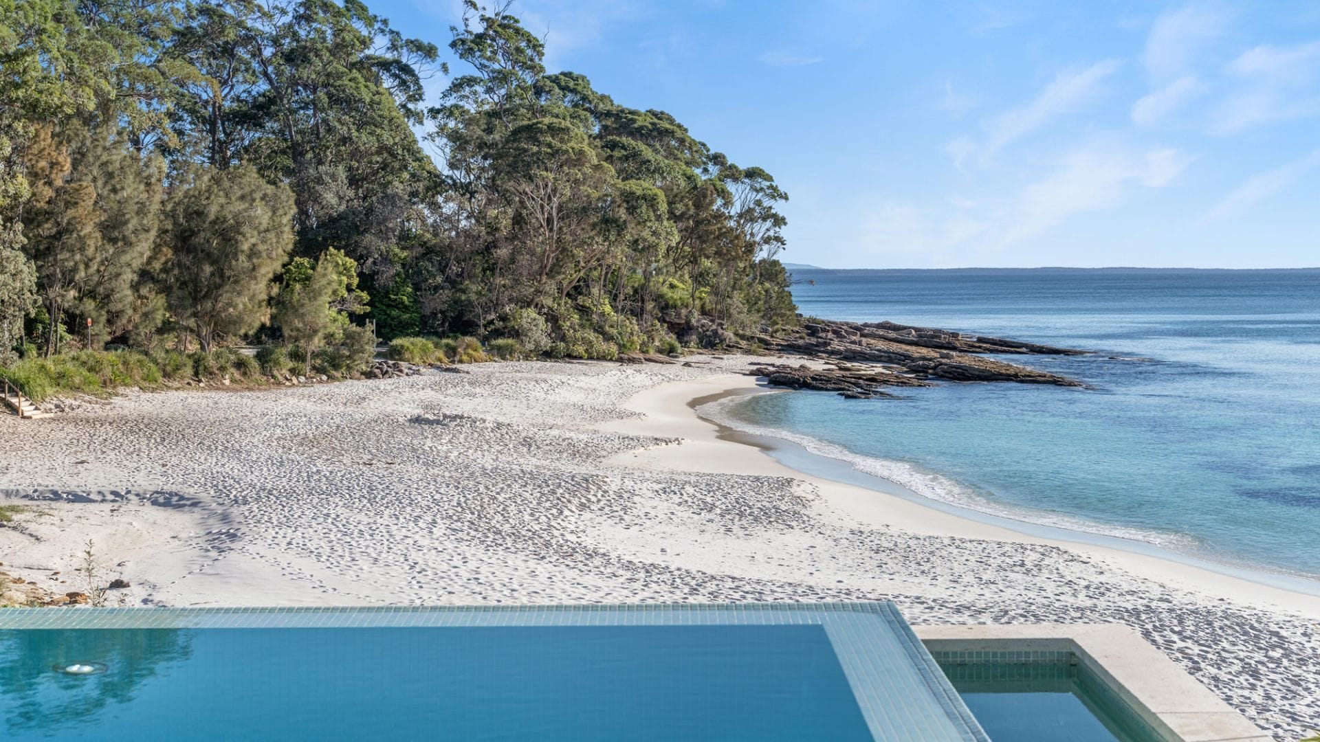 A beach with a pool, surrounded by trees and a rocky shoreline.