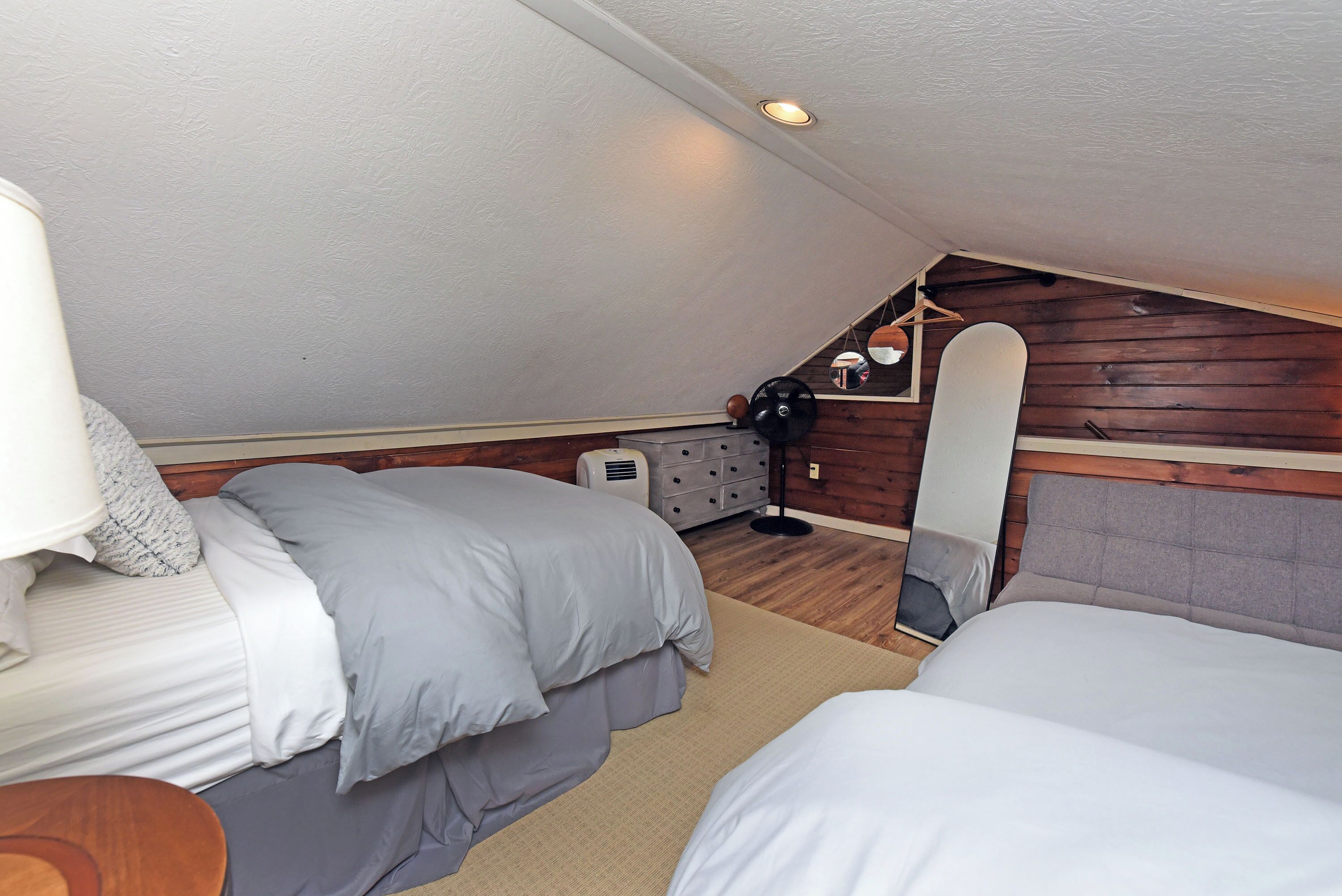 Een kleine, knusse slaapkamer met twee bedden, een dressoir, een spiegel en een plafondventilator.