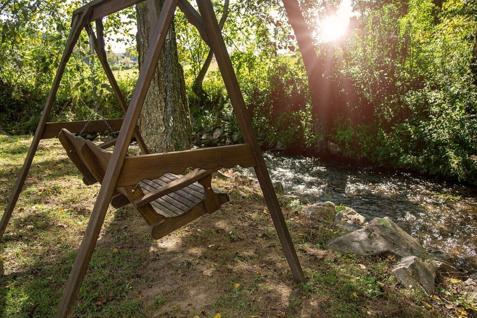 Un ensemble de balançoires en bois, installé dans un environnement naturel, avec un arbre et un ruisseau en arrière-plan.