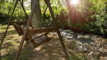 Un ensemble de balançoires en bois, installé dans un environnement naturel, avec un arbre et un ruisseau en arrière-plan.