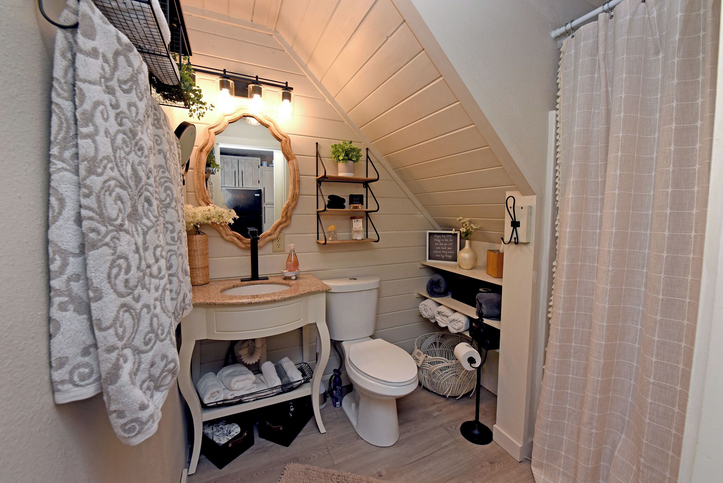 Une salle de bain avec un meuble-lavabo blanc, des toilettes, un miroir avec éclairage et un rideau de douche.