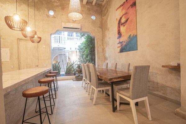 A dining area with a wooden table and chairs, a bar counter with stools, and a large window with a view of buildings and greenery.