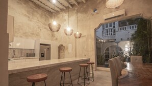 A modern kitchen with a marble countertop, bar stools, hanging pendant lights, and a view of a balcony. - 7 Bedroom Beautiful Mansion in the Old City (Cartagena)