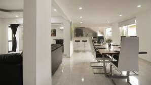 Una cocina moderna con comedor, que incluye una mesa larga con sillas, un sofá y una barra con taburetes.