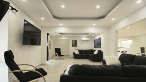 Una sala de estar moderna con un televisor de pantalla plana, sofás negros, un sillón mecedor y obras de arte en las paredes.