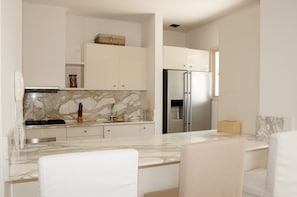 A modern kitchen with marble countertops, stainless steel appliances, and white cabinetry.